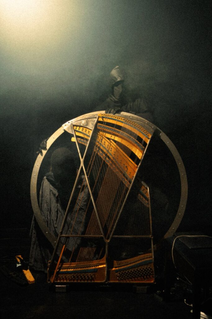 Vertical documentation with harp-like object and masked performer